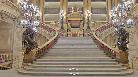 Bạn đang ở bên trong nhà hát Garnier, dưới chân cầu thang lớn có bậc được chế tác bằng mã não và cẩm thạch. Trước khi bước lên cầu thang, bạn hãy ngắm những bức tượng và các tác phẩm mạ vàng
